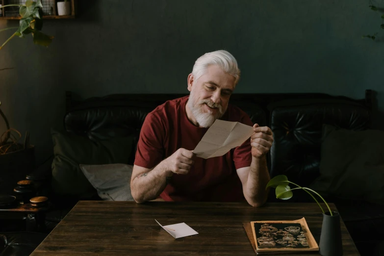 an older man sitting at a wooden table holding a paper