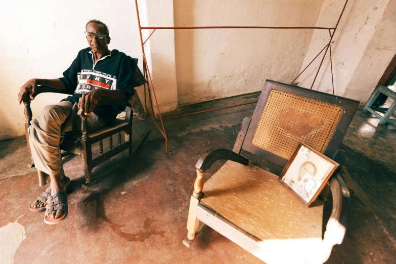 man sitting in chair and framed pograph next to leaning wall