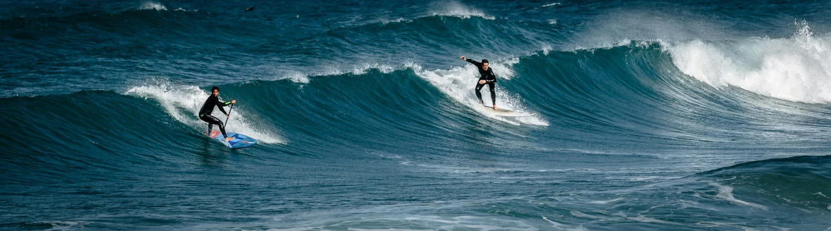 two people are surfing in the ocean with large waves