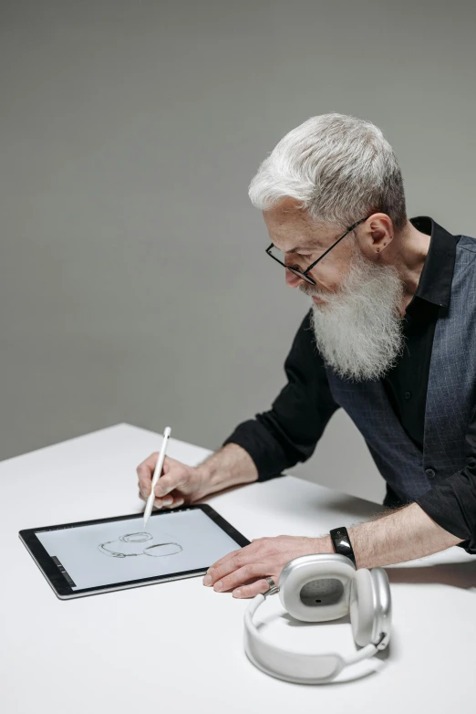 an older man sitting at a desk using a tablet and electronic device