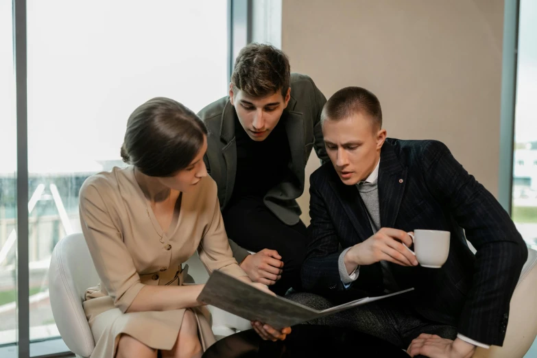 the two young men and one woman are looking at a folder