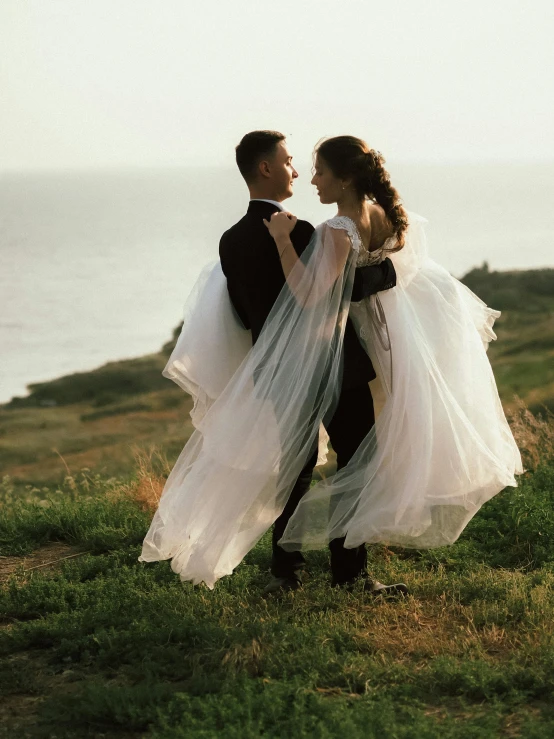 a bride and groom are standing on a grassy hill in the sunset