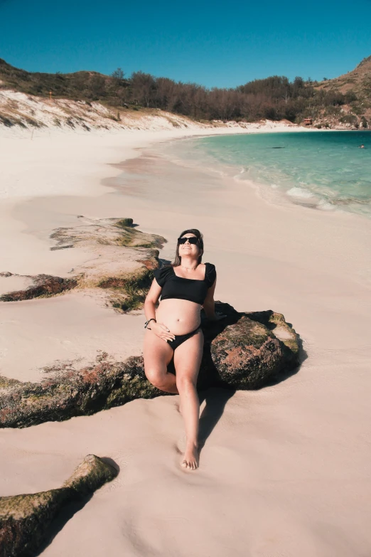 a pregnant woman sitting on a log at a beach