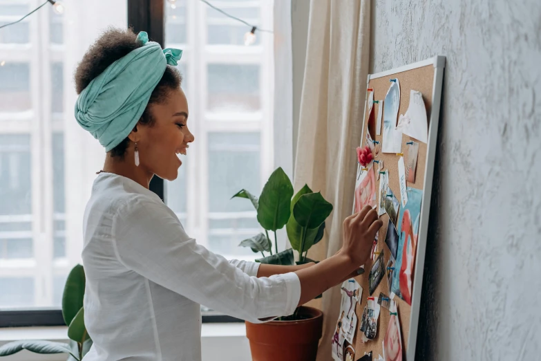 a woman placing images on a bulletin board with plants in front of her