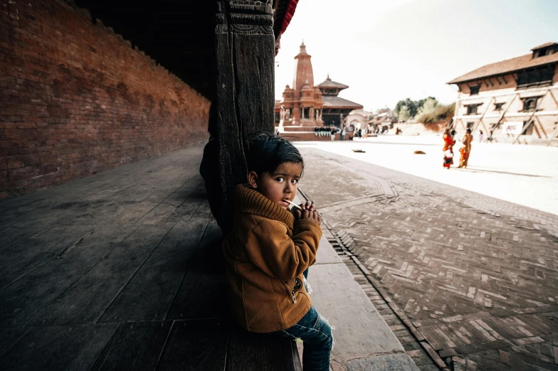 little boy in yellow jacket leaning on building