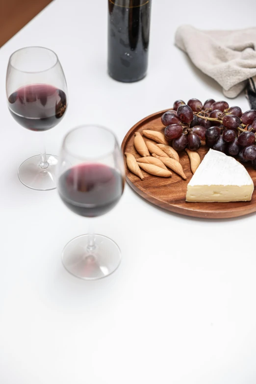 two glasses of wine sit next to an assortment of foods and cheese