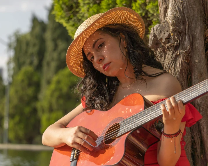 a beautiful young lady holding a guitar standing in front of a tree