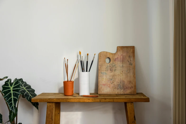 a table with paint brushes, vases and an unfinished piece of wood