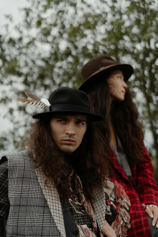 two men in hats standing together in front of trees