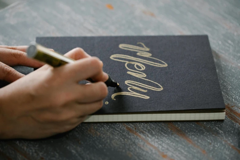 a person writing on a notebook in gold foil