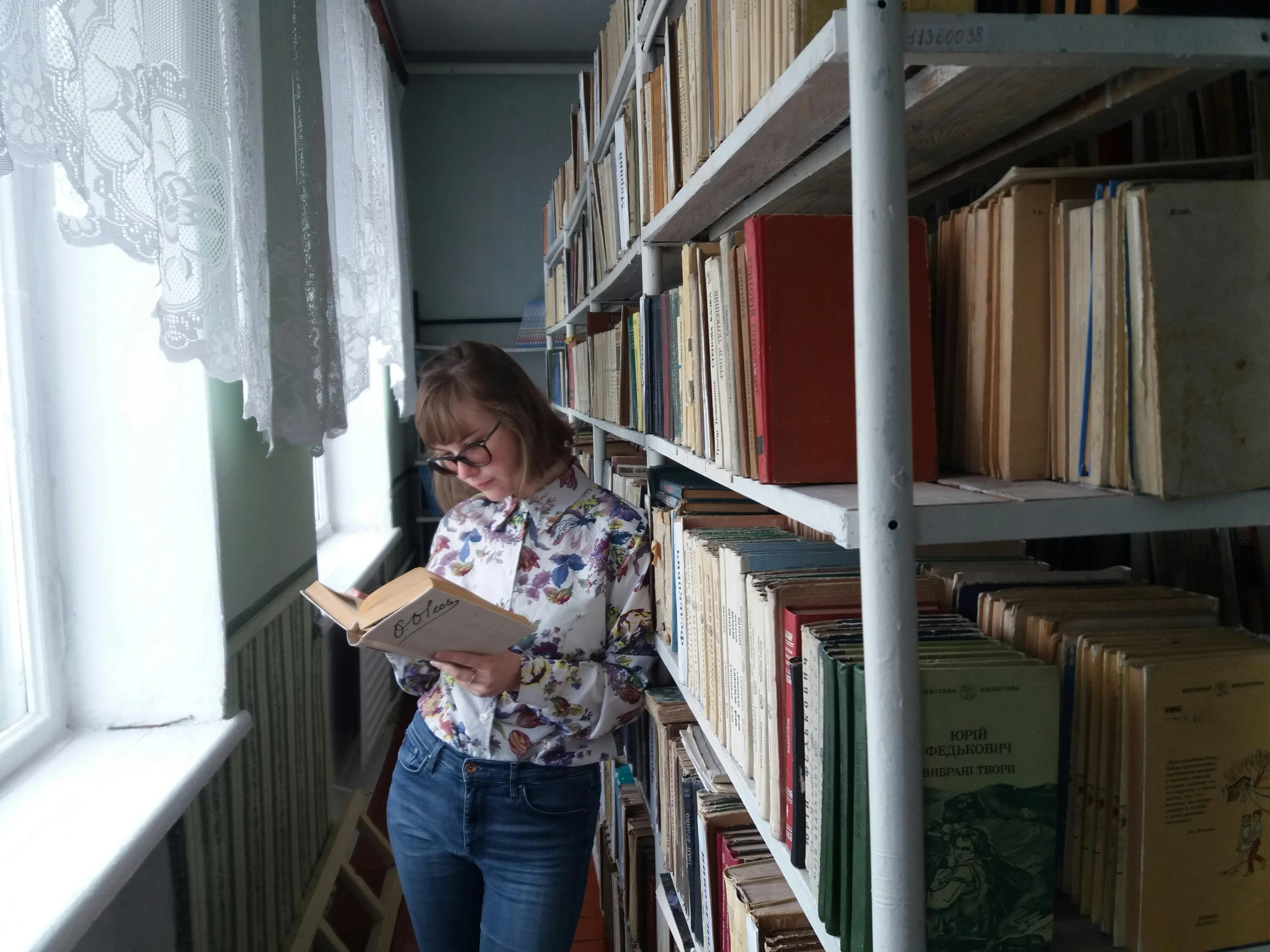 a woman is holding an open book next to a shelf full of books