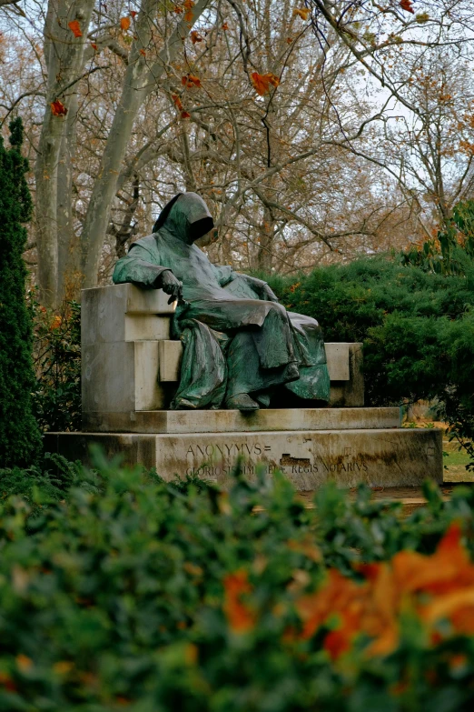 the bronze statue is sitting on a stone slab in the middle of trees