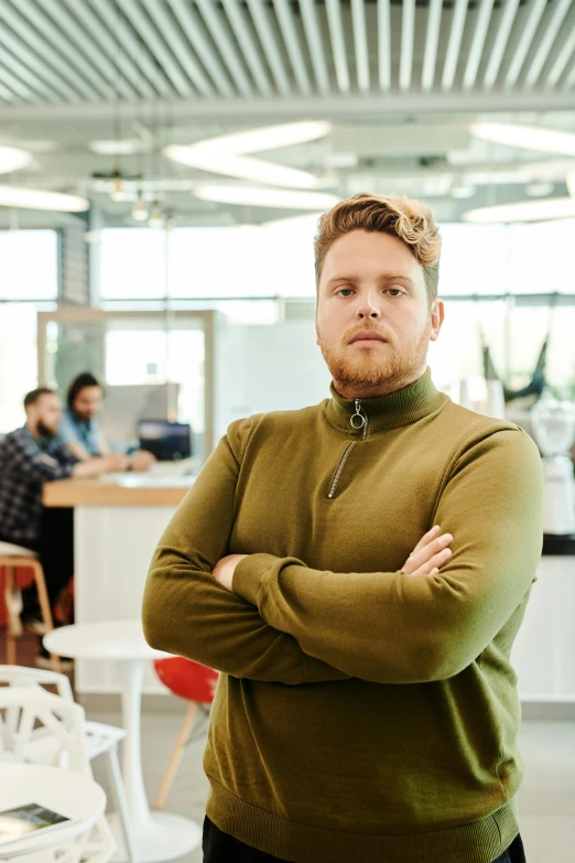 a man is standing with his arms crossed, wearing a sweater