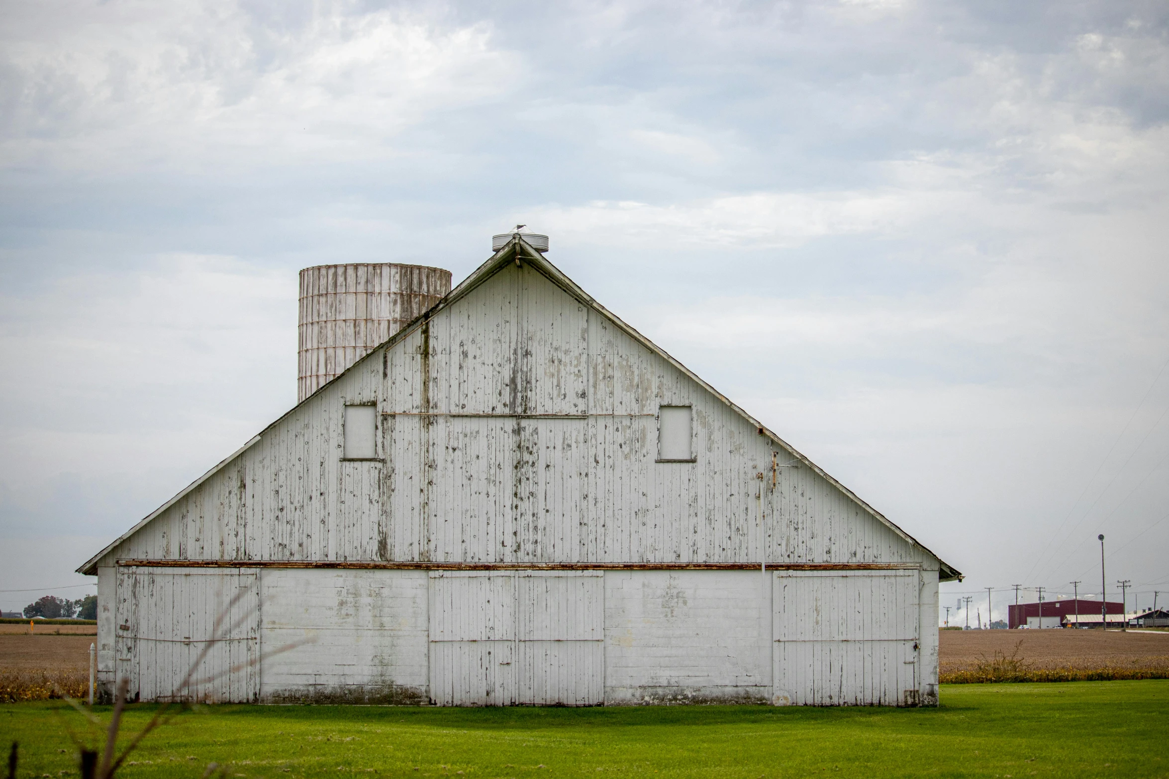 a white barn with two silos sits in an open field