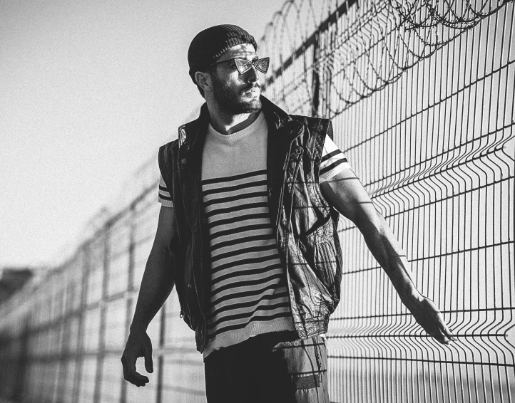 a man in a striped shirt and vest stands next to a fence