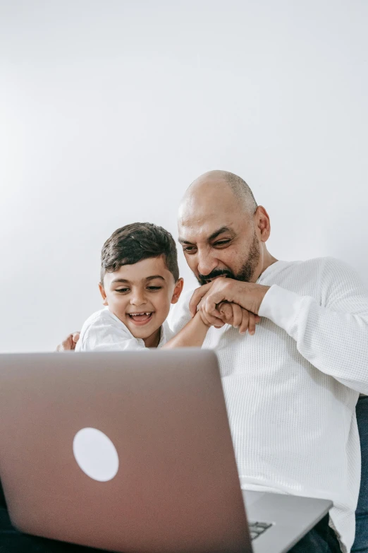 a man sitting next to his son who is using a laptop