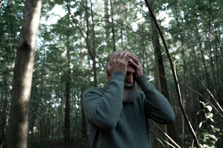 a man holds his hand over the face and stares through trees