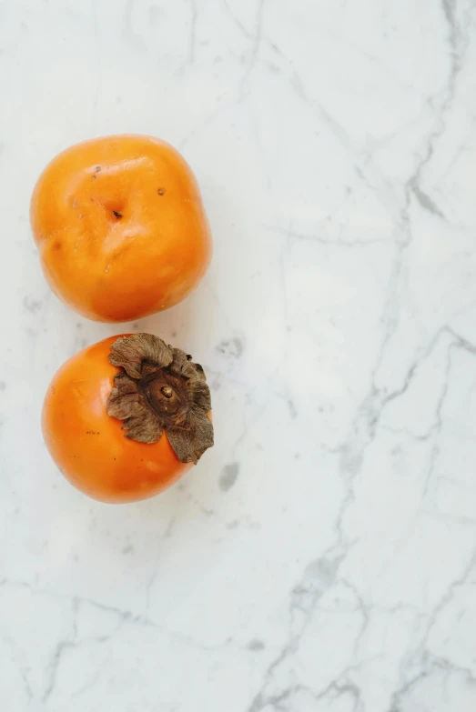 two oranges sitting on a table top, one with a leaf