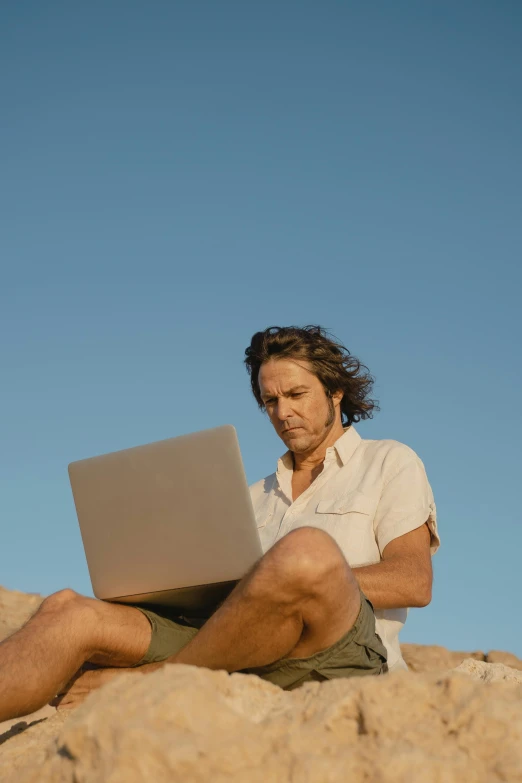 a man sitting on top of a rocky hill using a laptop