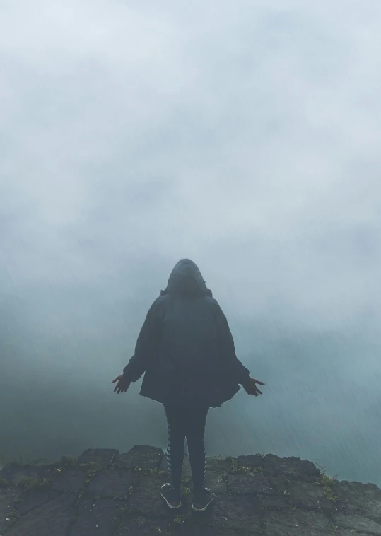 a person standing in the rain while looking out at a cliff