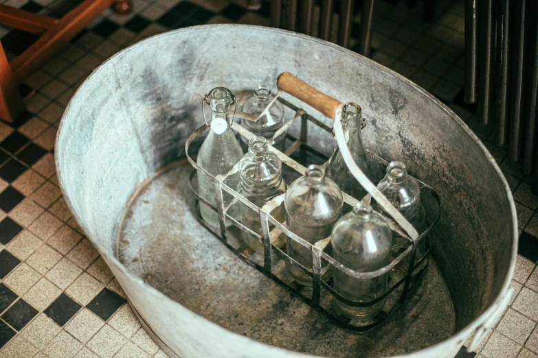 an old and rusty metal bucket with six small empty glass bottles in it