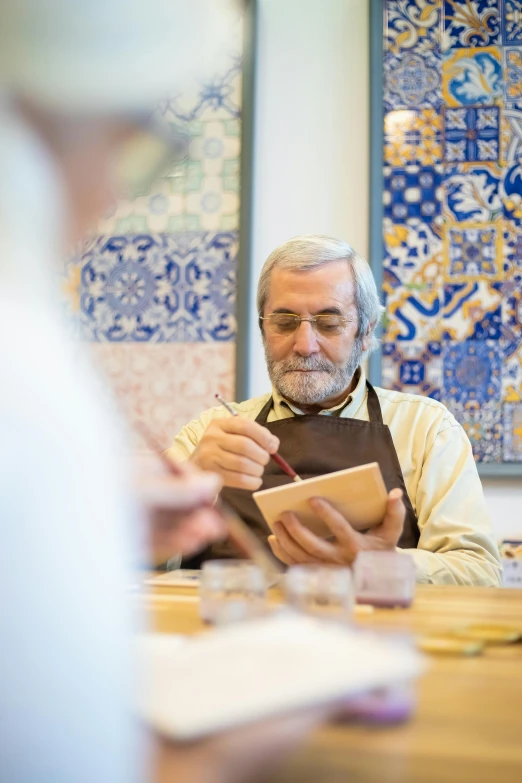 an old man sitting at a table writing on a piece of paper