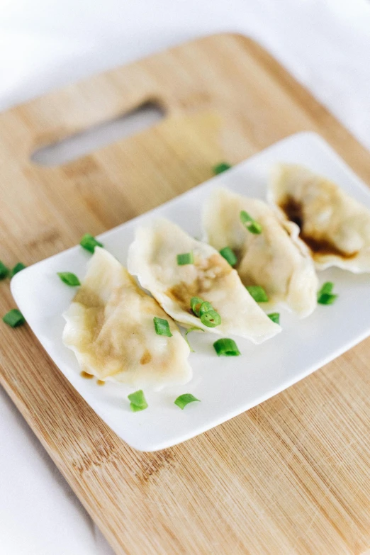 some dumplings on a small white plate and green onions