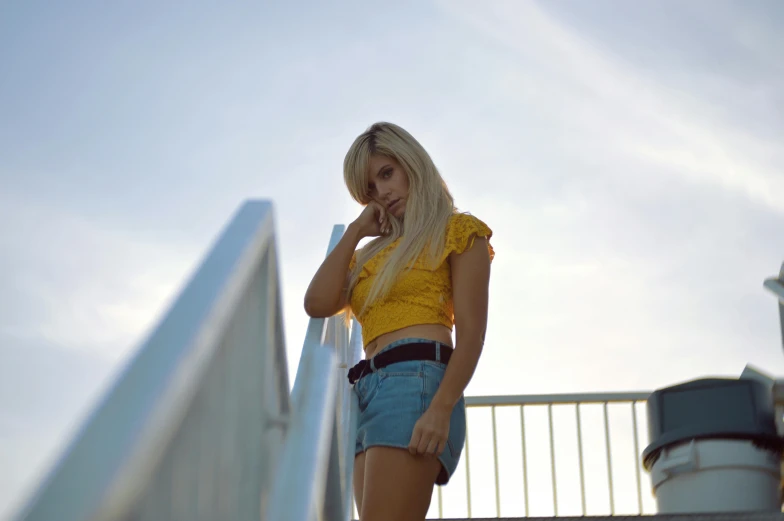 a young blond woman wearing blue shorts standing next to a railing