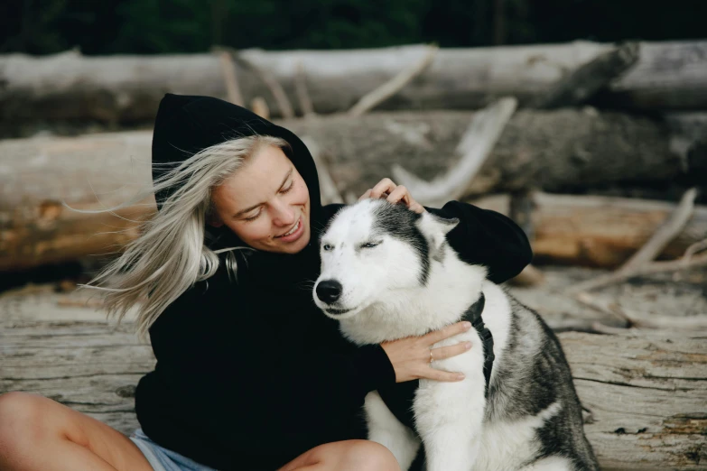 a woman hugging a husky dog on a log covered ground