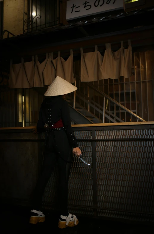 a person standing against a fence holding a hat