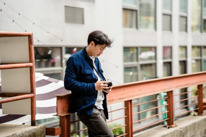 the man is leaning on a railing looking at his cell phone