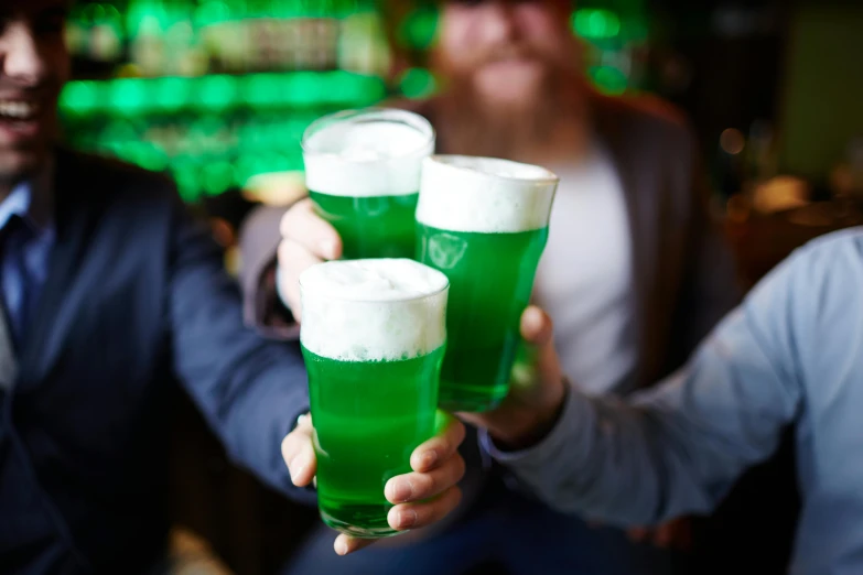 three men holding up green glasses of liquid