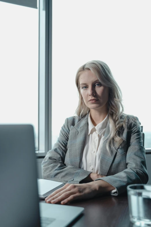 a woman in a suit sitting at a desk near a laptop