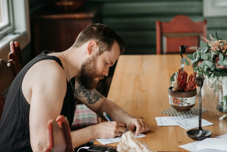 a bearded man is sitting at a table writing