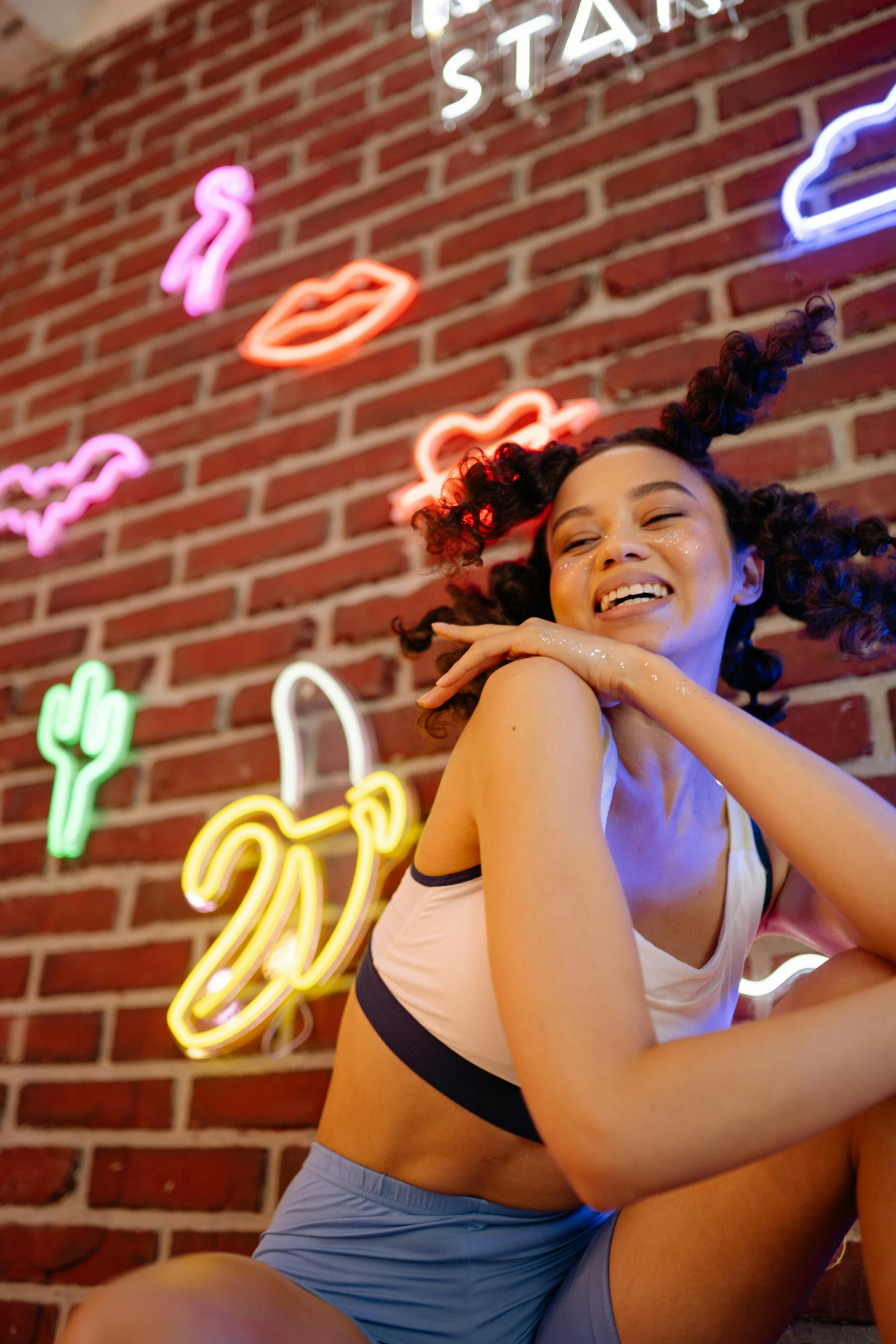 a smiling young woman leaning against a brick wall and holding onto an armband