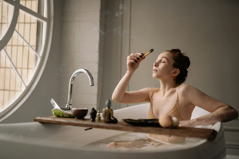 a woman sitting in a bathtub with thermometer in her mouth