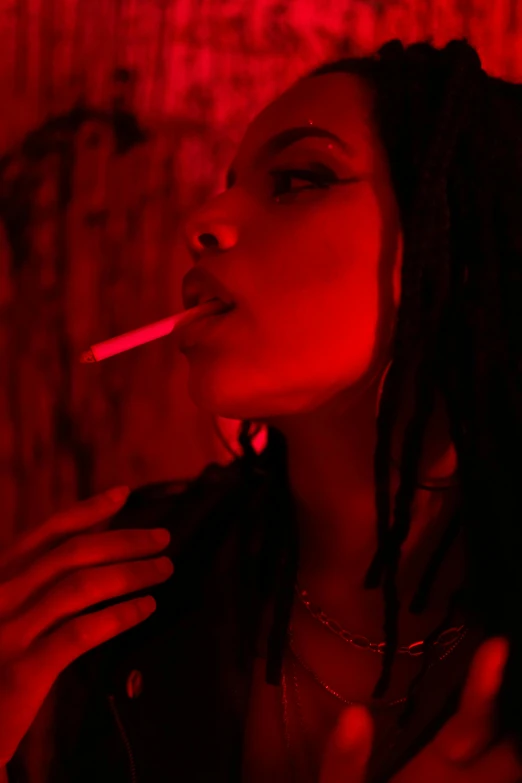 woman smoking in red light with dreadlocks in a darkened room