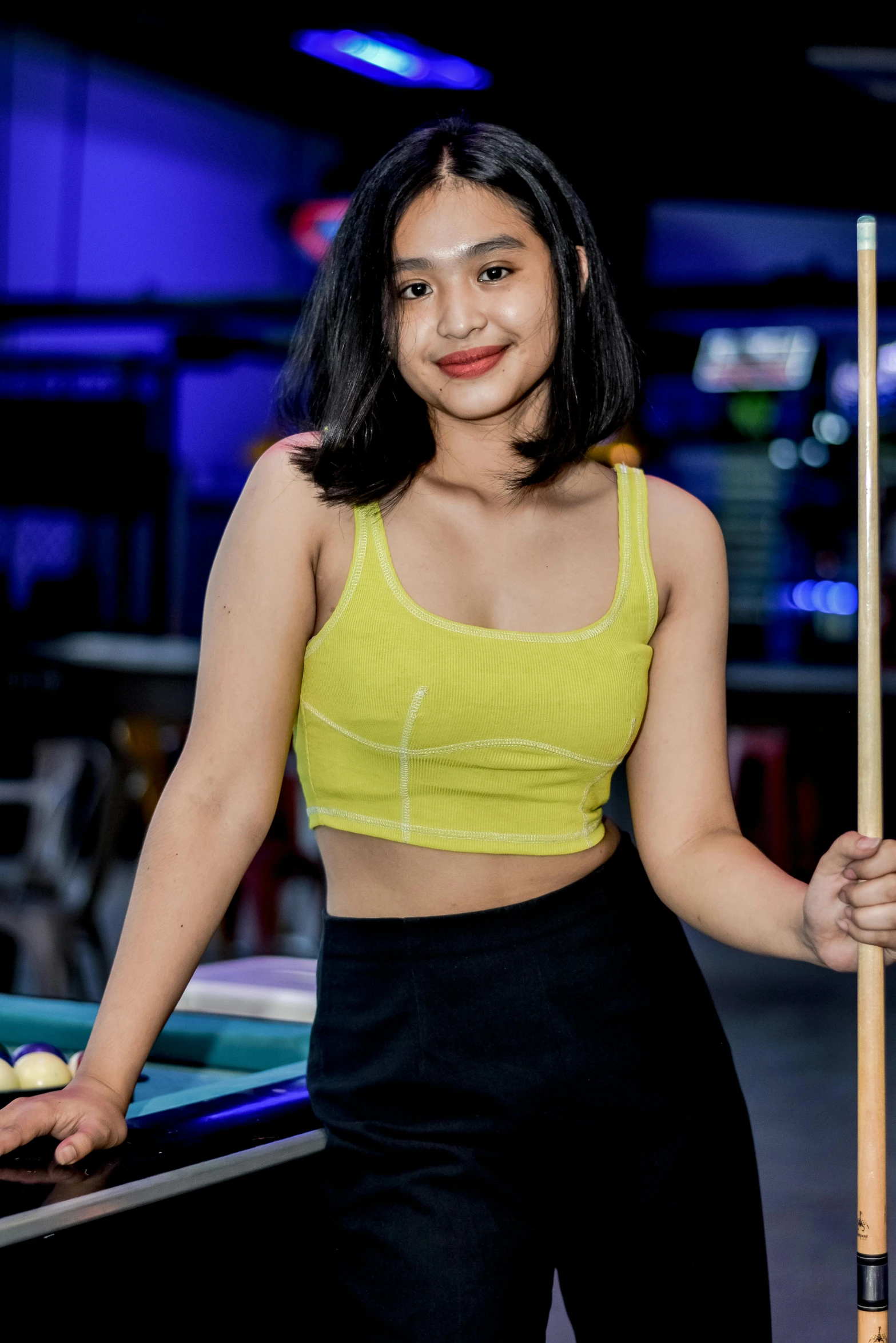 a woman in a yellow top is holding a pool stick