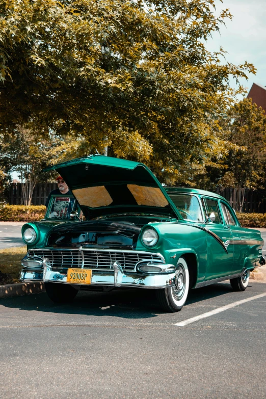 a green car is parked in a lot next to trees