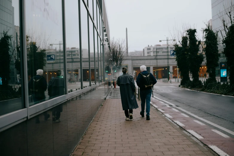 two people walk down the sidewalk near some buildings