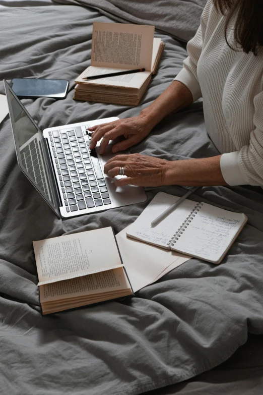 a person with their hand on a laptop, while holding several books