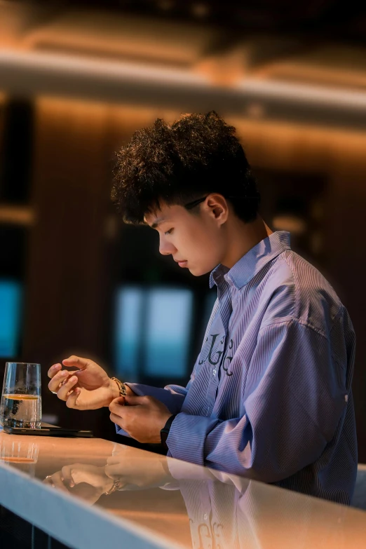 a boy is sitting at a counter writing on his cellphone