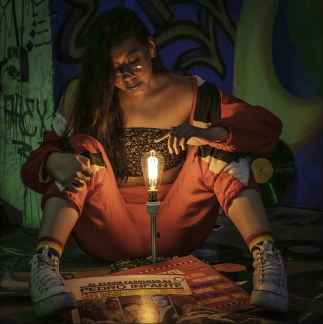 a girl sits with her legs crossed on the floor and a lit candle is in her lap as she looks at the book