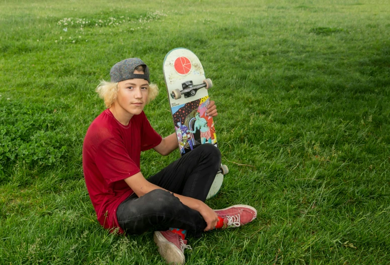 a boy holding a skateboard on green grass