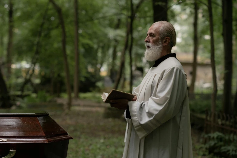 a man holding a book in his hand standing in a park