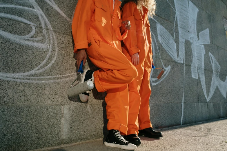 two men in orange jumpsuits posing against a wall