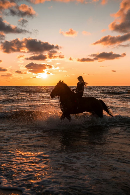 a horse and rider running through the ocean as the sun sets