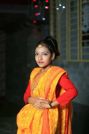 the little girl with bright orange sari is posing for the camera