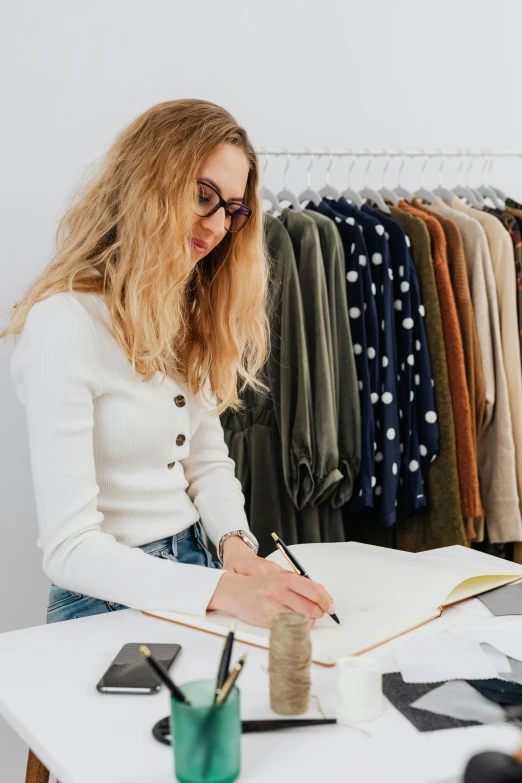 the woman is writing in her notebook by some clothes