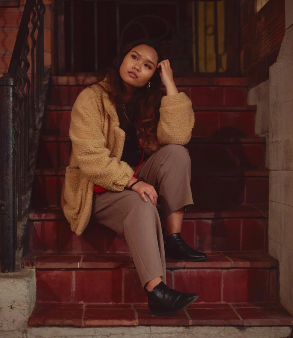 a woman sitting on steps wearing a brown jacket